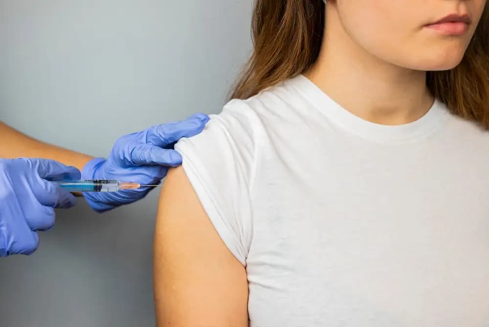 A clinician in gloves giving a vitamin injection in the upper arm