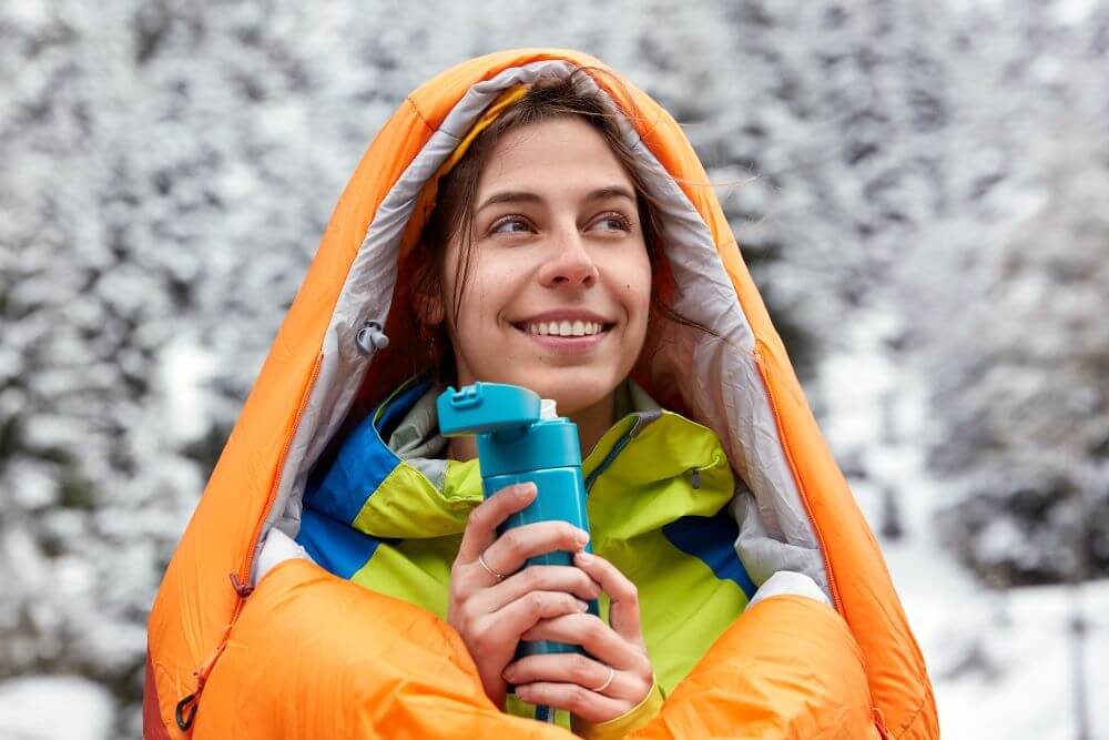 satisfied European woman wears swimming bag travels snowy mountains holds flask hot drink